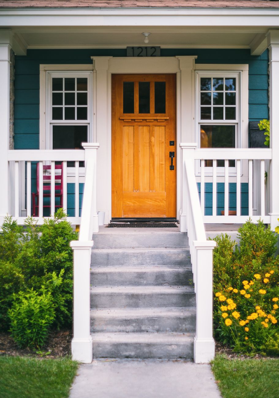 A front porch with a wooden door, the house number above it, a clear path and steps, and planting on both sides