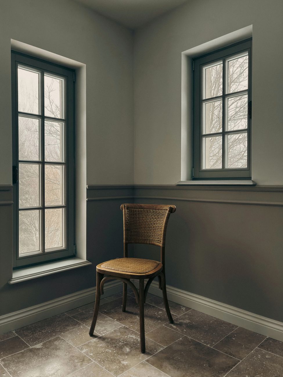 A quiet corner of a room with two tall windows, painted walls and a single wooden chair